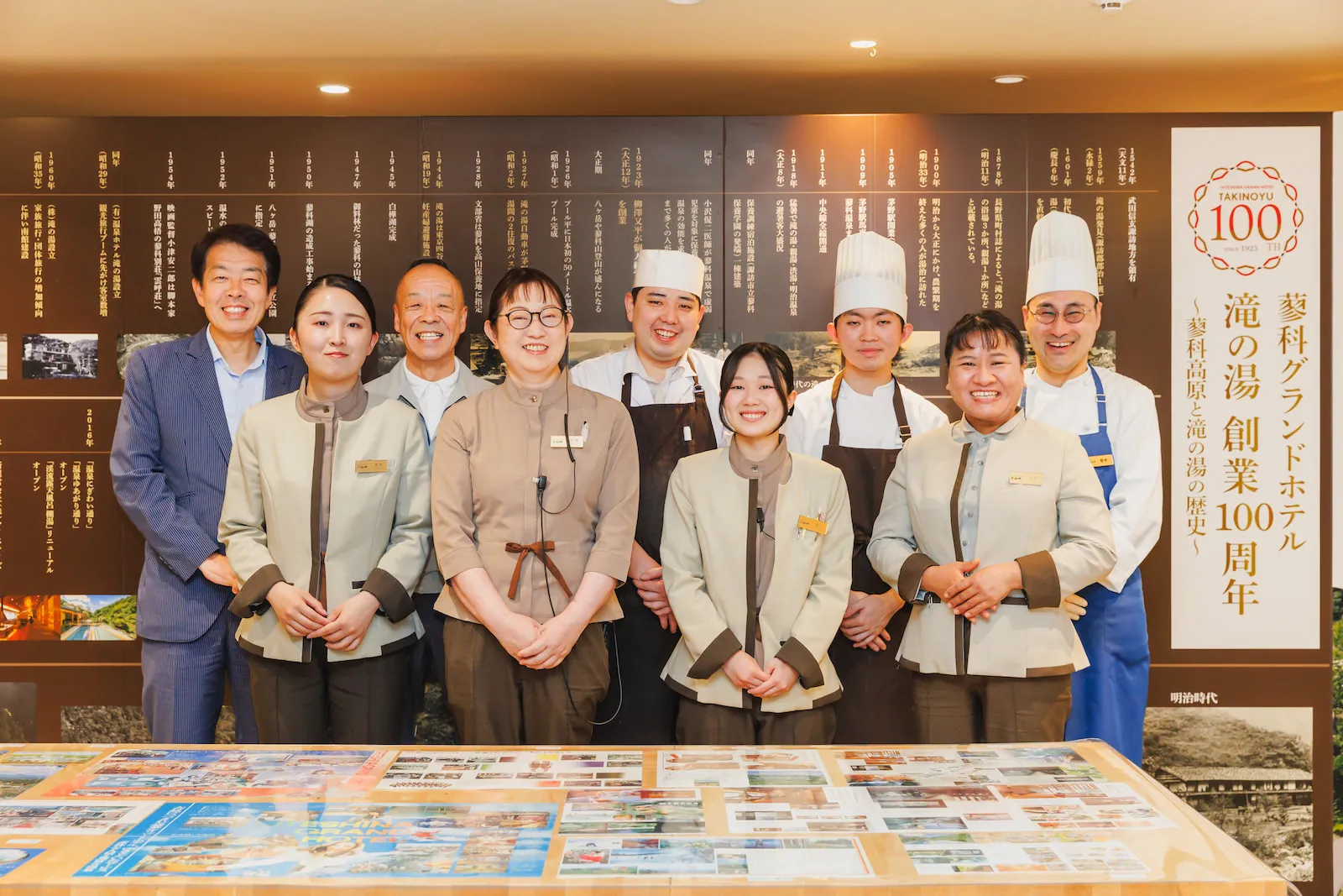創業100周年の歴史展示の前に立つ、接客・料理など様々な職種のスタッフ